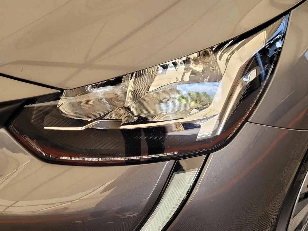 Gros plan sur le phare avant droit d'une Peugeot 208 gris foncé 2023 avec détails LED et carrosserie brillante