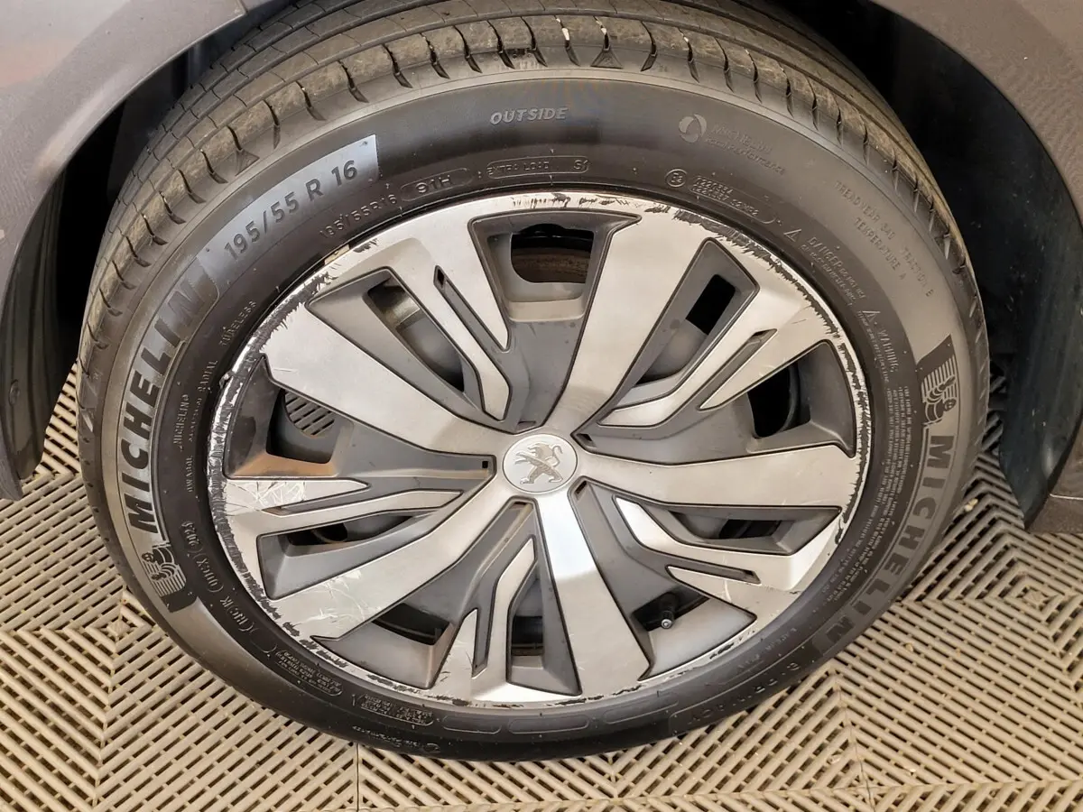 Gros plan sur la jante avant droite gris argenté d'une Peugeot 208 gris foncé avec logo lion central.