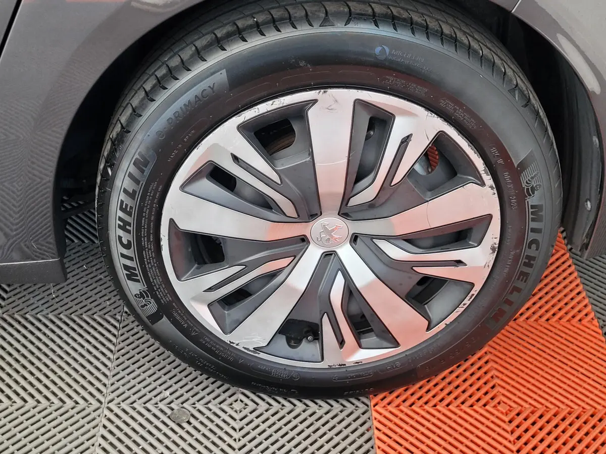 Gros plan sur la roue avant droite d'une Peugeot 208 gris foncé, mettant en valeur la jante et le pneu Michelin.