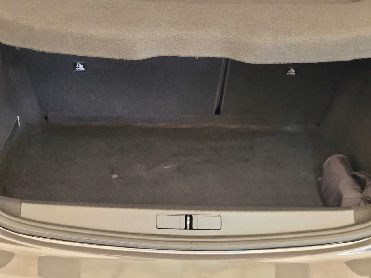 Coffre ouvert d'une Peugeot 208 gris foncé, vue de l'arrière montrant l'espace de chargement vide et la moquette noire.