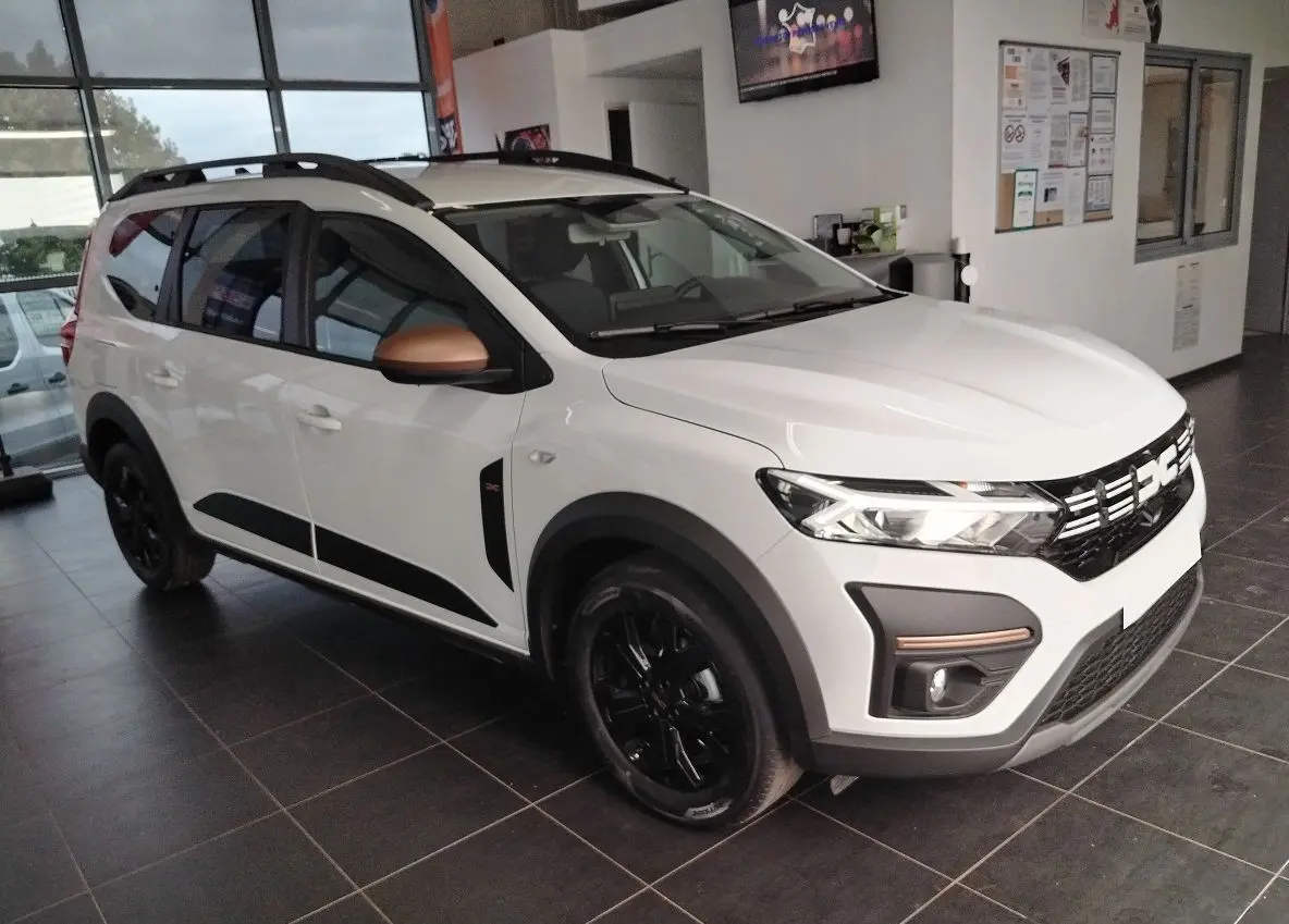 Vue 3/4 avant d'un Dacia Jogger blanc avec rétroviseurs cuivrés et jantes noires en showroom.