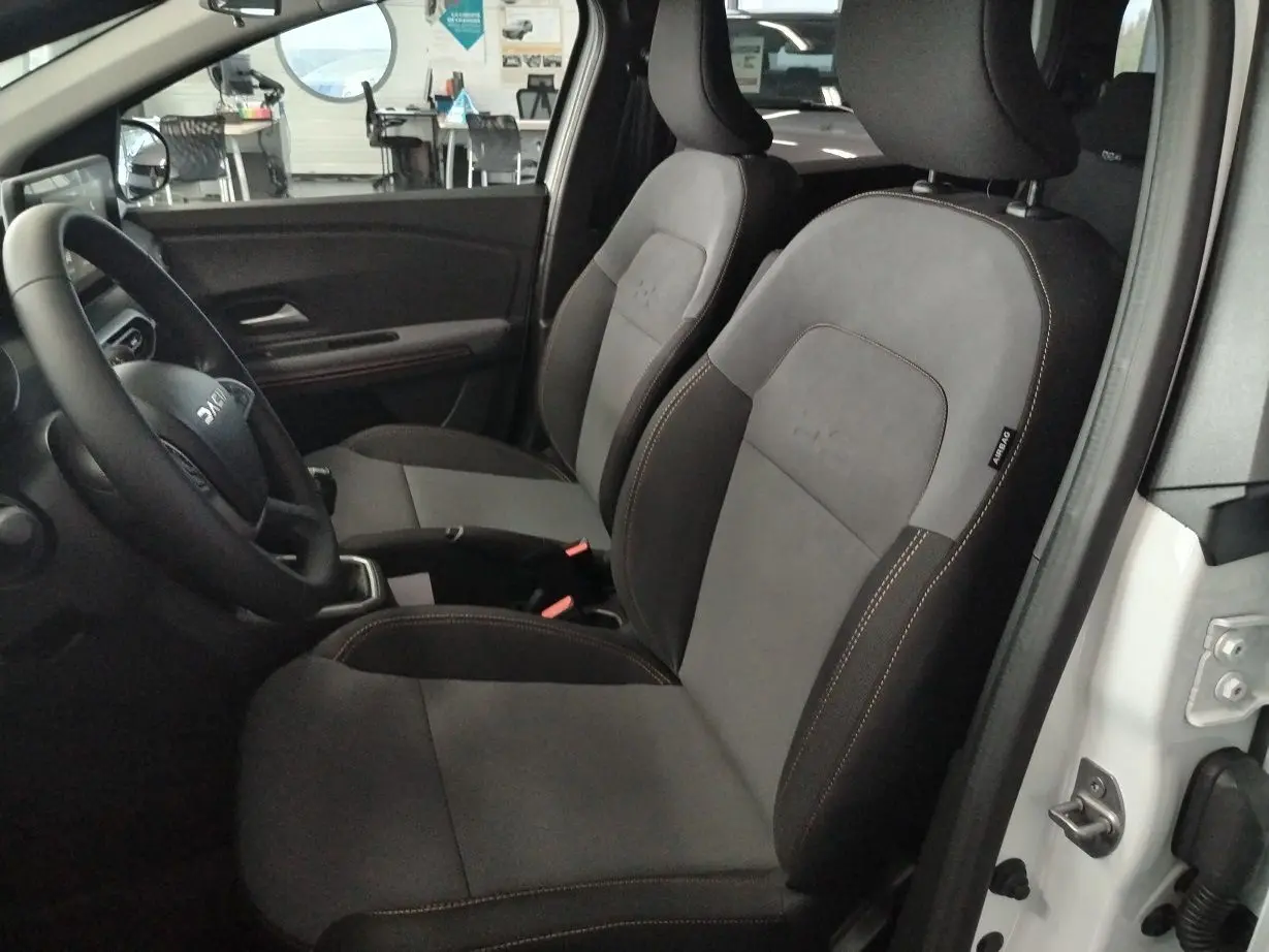 Vue intérieure côté conducteur du Dacia Jogger blanc 2025, sièges bi-matière gris et noir avec surpiqûres contrastantes.