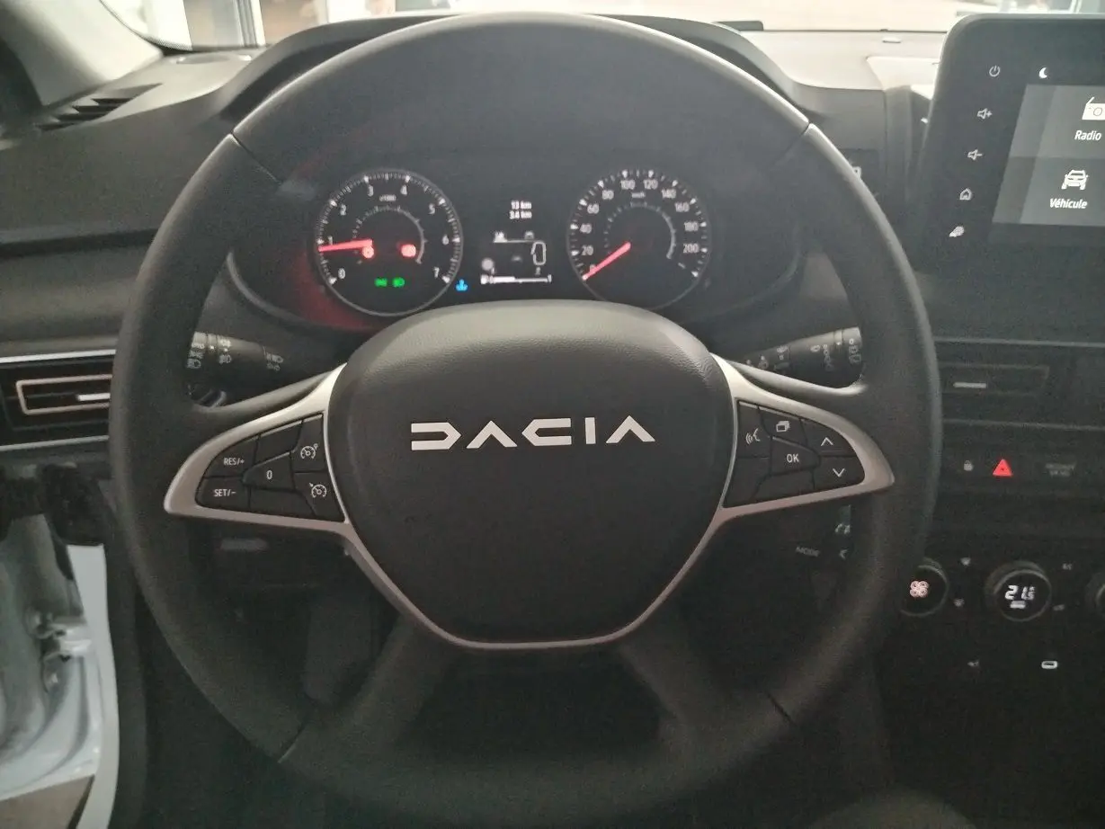 Vue rapprochée du volant noir DACIA avec commandes intégrées et tableau de bord numérique du Jogger blanc 2025.