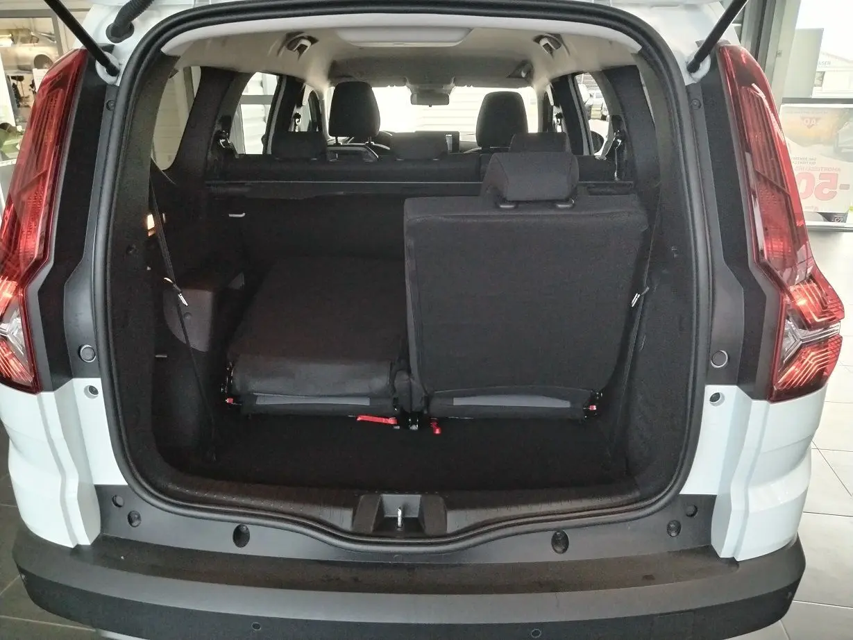 Vue arrière du coffre ouvert d'un Dacia Jogger blanc 2025, montrant les sièges arrière partiellement rabattus.