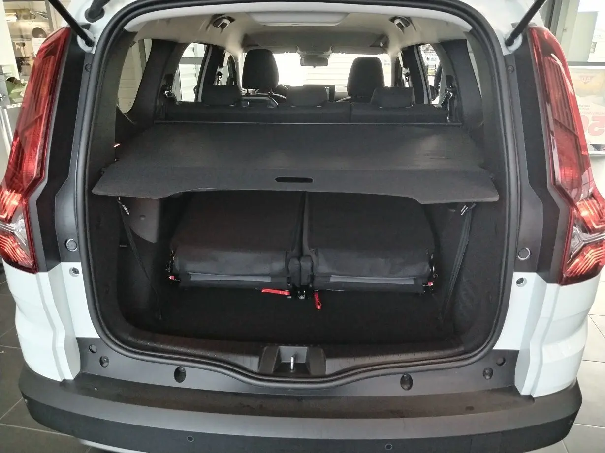Vue arrière ouverte du coffre du Dacia Jogger blanc 2025, montrant la tablette cache-bagages et les sièges rabattus.