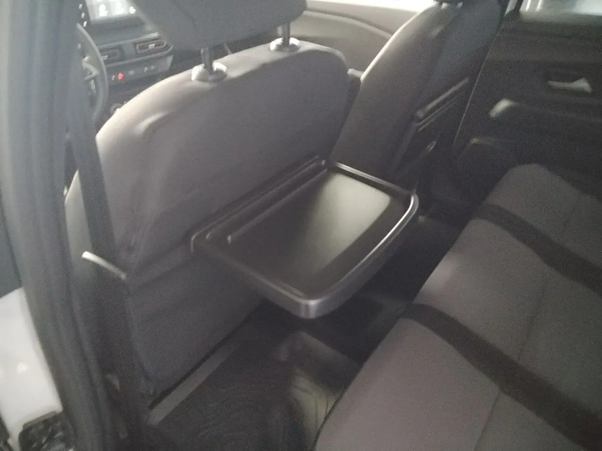 Vue intérieure arrière droite du Dacia Jogger blanc 2025, mettant en valeur la tablette rabattable sur le siège avant.