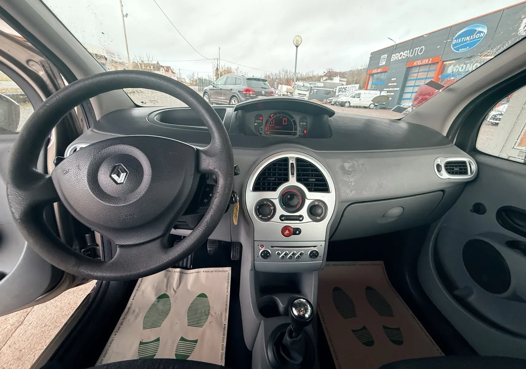 Vue intérieure avant de la Renault Modus beige, montrant le volant, tableau de bord et levier de vitesse manuel.