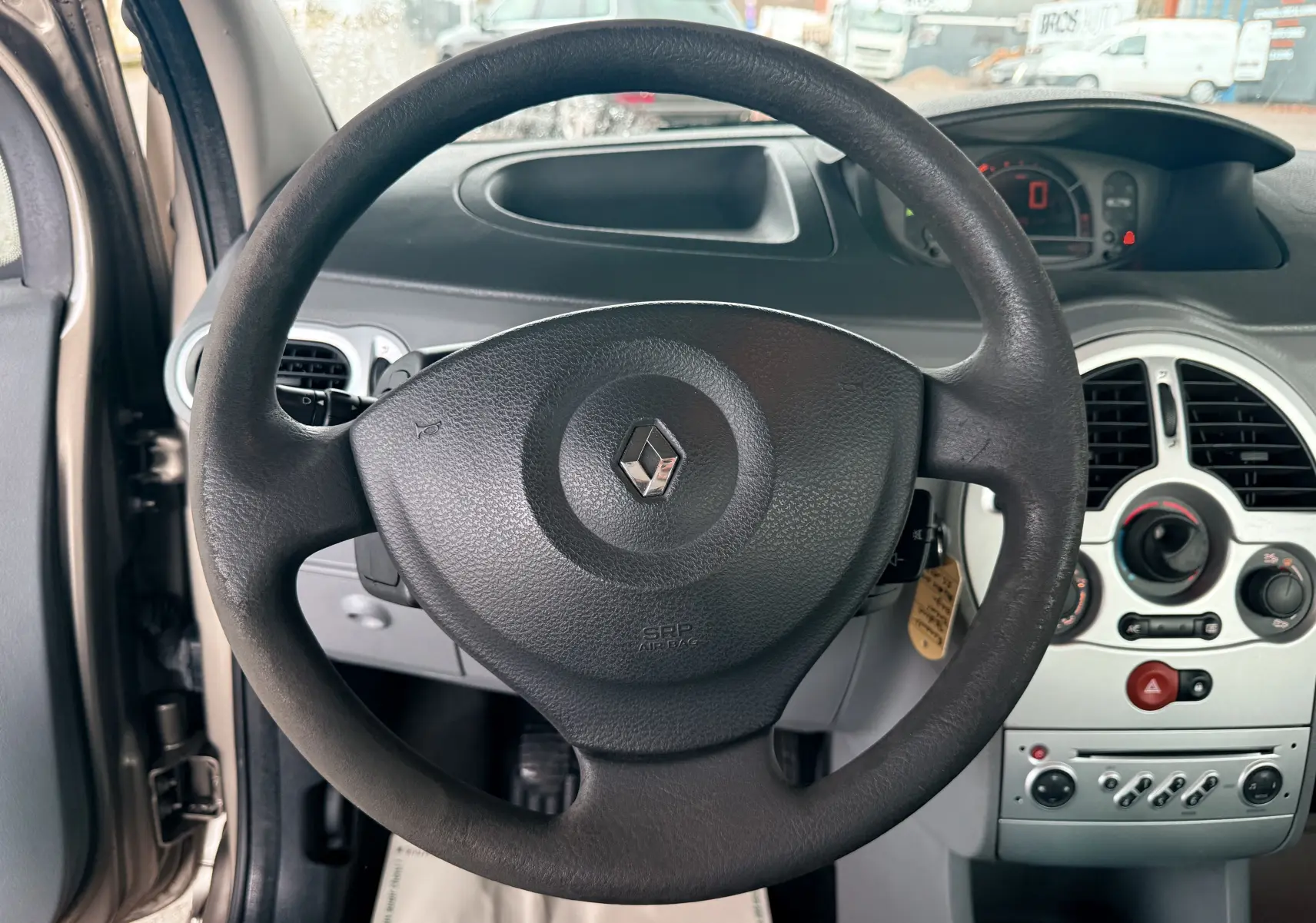 Vue centrée sur le volant noir avec logo Renault, tableau de bord et console centrale d’une Renault Modus beige 2011.