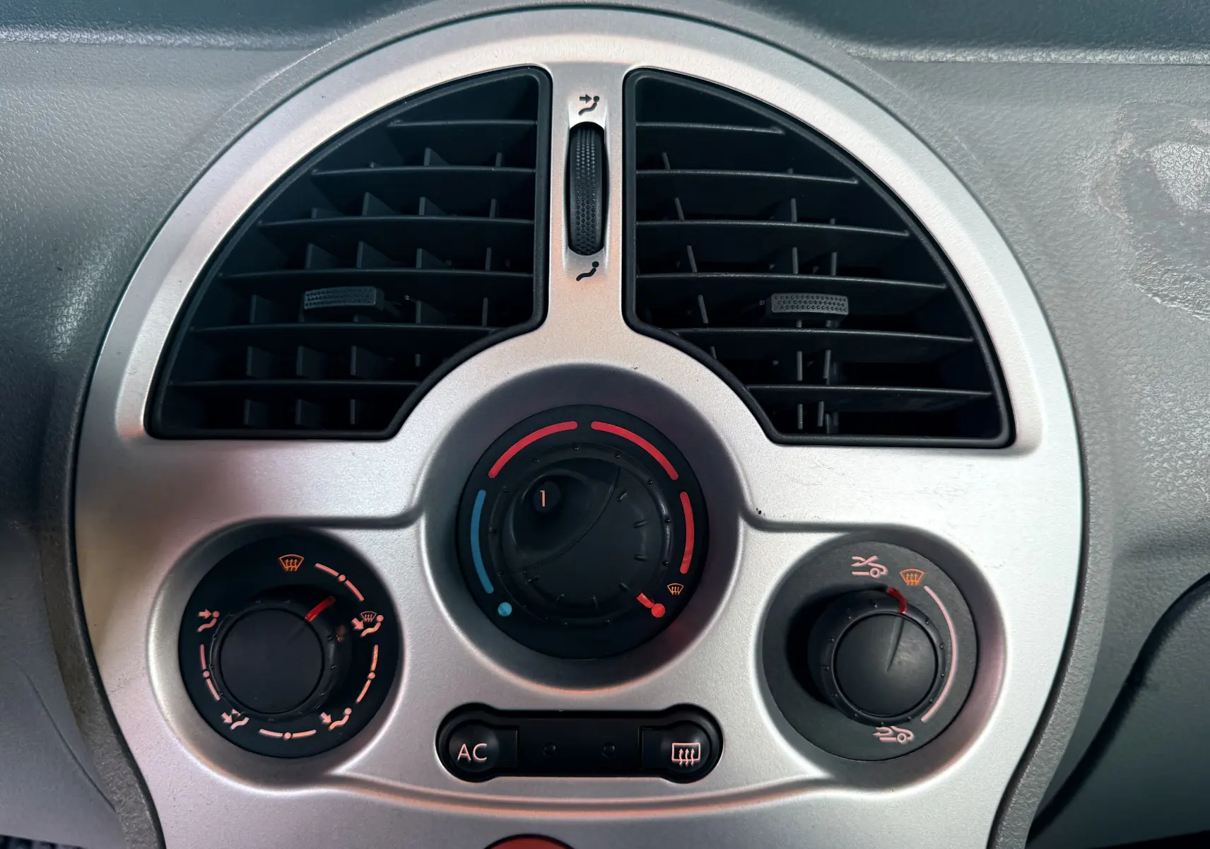 Gros plan sur la sortie d'air centrale ronde et la commande de chauffage du tableau de bord gris du Renault Modus beige.