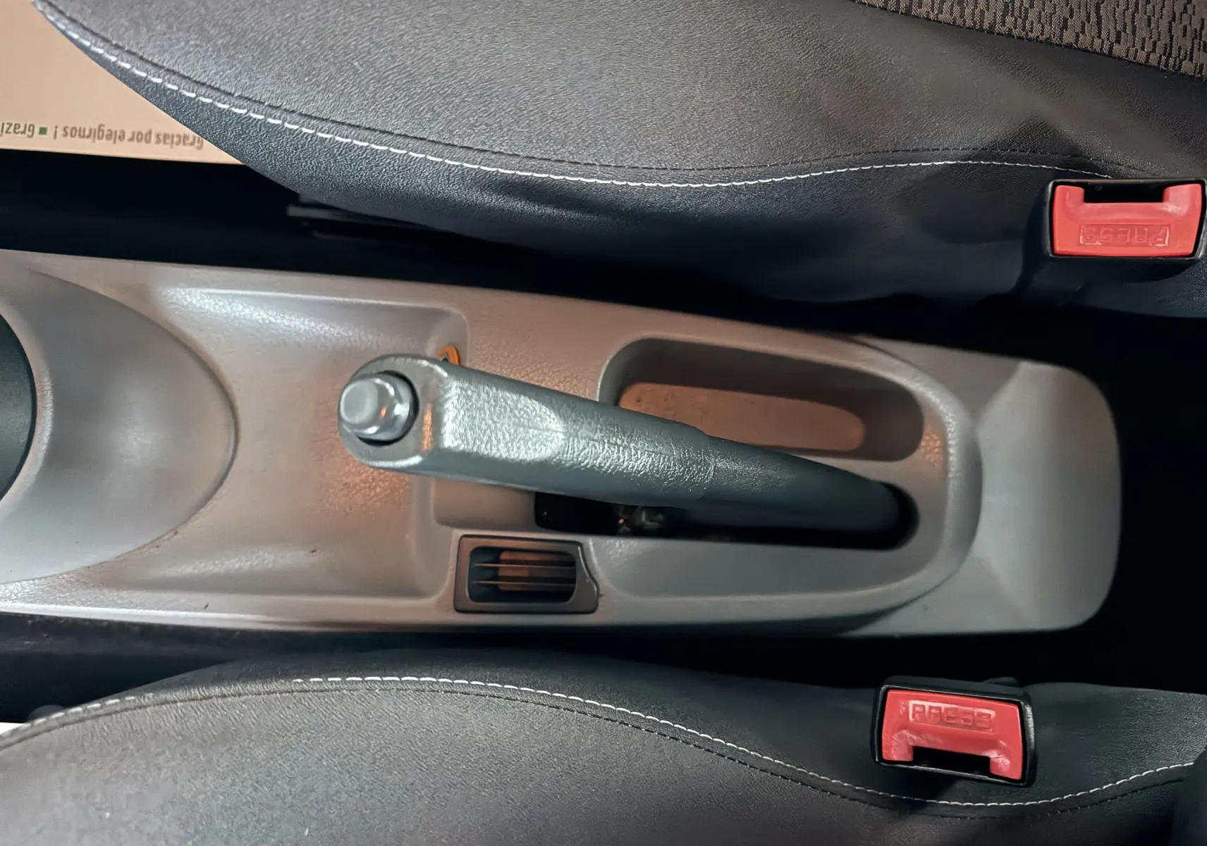 Vue rapprochée de la poignée de frein à main grise entre deux sièges tissu gris-noir d’une Renault Modus beige de 2011.