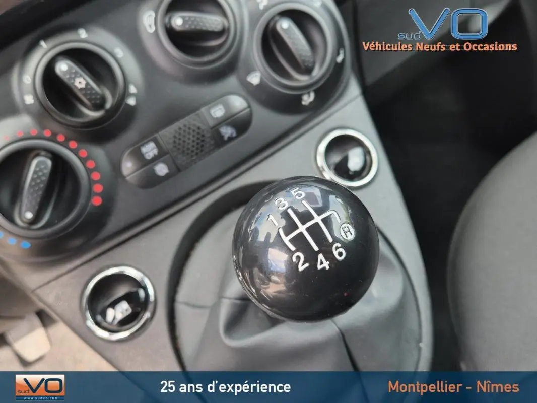 Gros plan sur le levier de vitesses manuel noir de la FIAT 500C 2024, avec commandes de climatisation en arrière-plan.