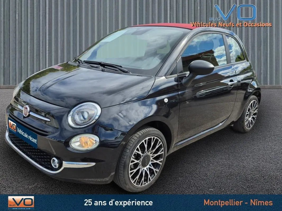 Vue 3/4 avant droite d'une FIAT 500C noire 2024 avec jantes alliage et toit rouge, stationnée sur sol goudronné.