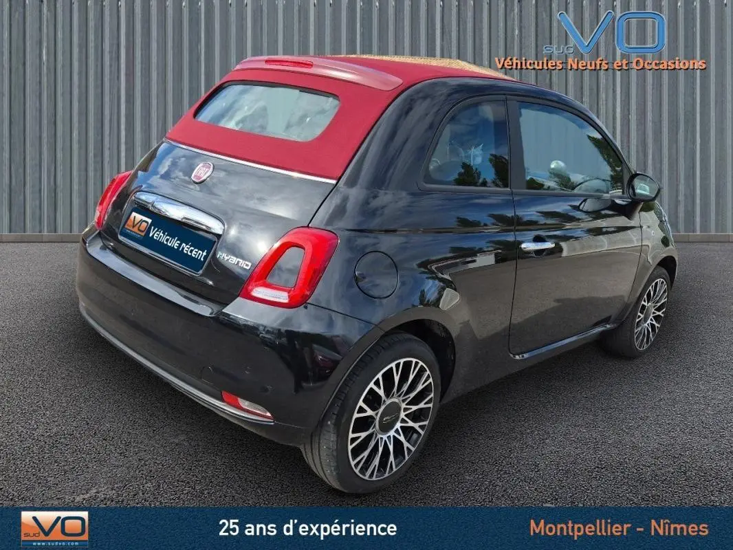 Vue 3/4 arrière droite d'une FIAT 500C noire 2024 avec toit rouge et jantes alliage, version hybride essence avec roue de secours.