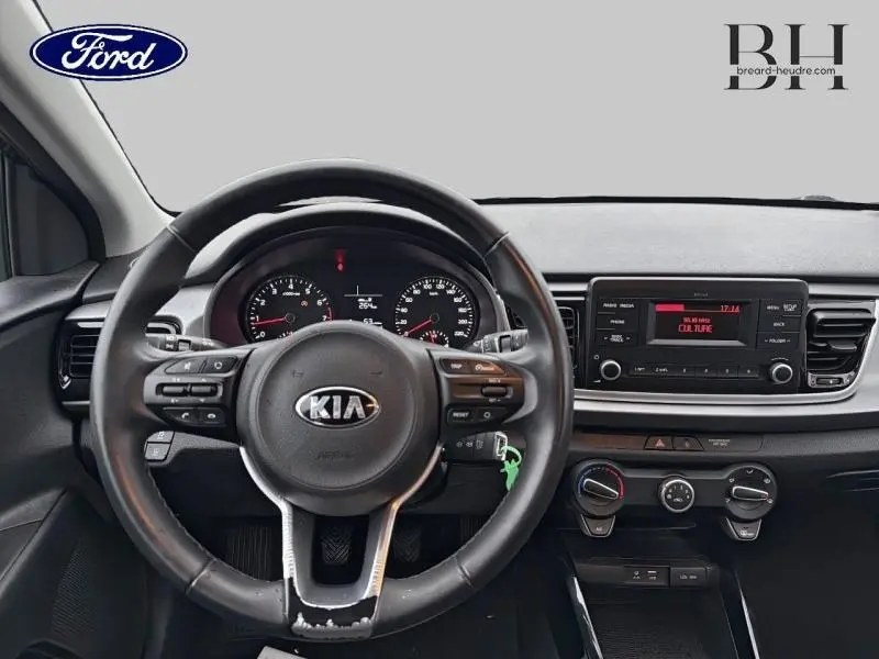 Vue intérieure centrée sur le volant cuir noir d'une KIA Rio 2018 avec tableau de bord et console centrale visibles.