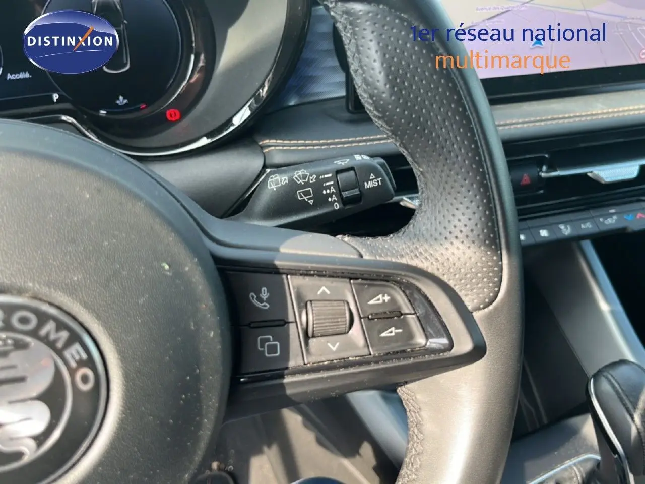 Gros plan sur le volant en cuir perforé noir de l'Alfa Romeo Tonale 2023, avec commandes intégrées et tableau de bord partiel.