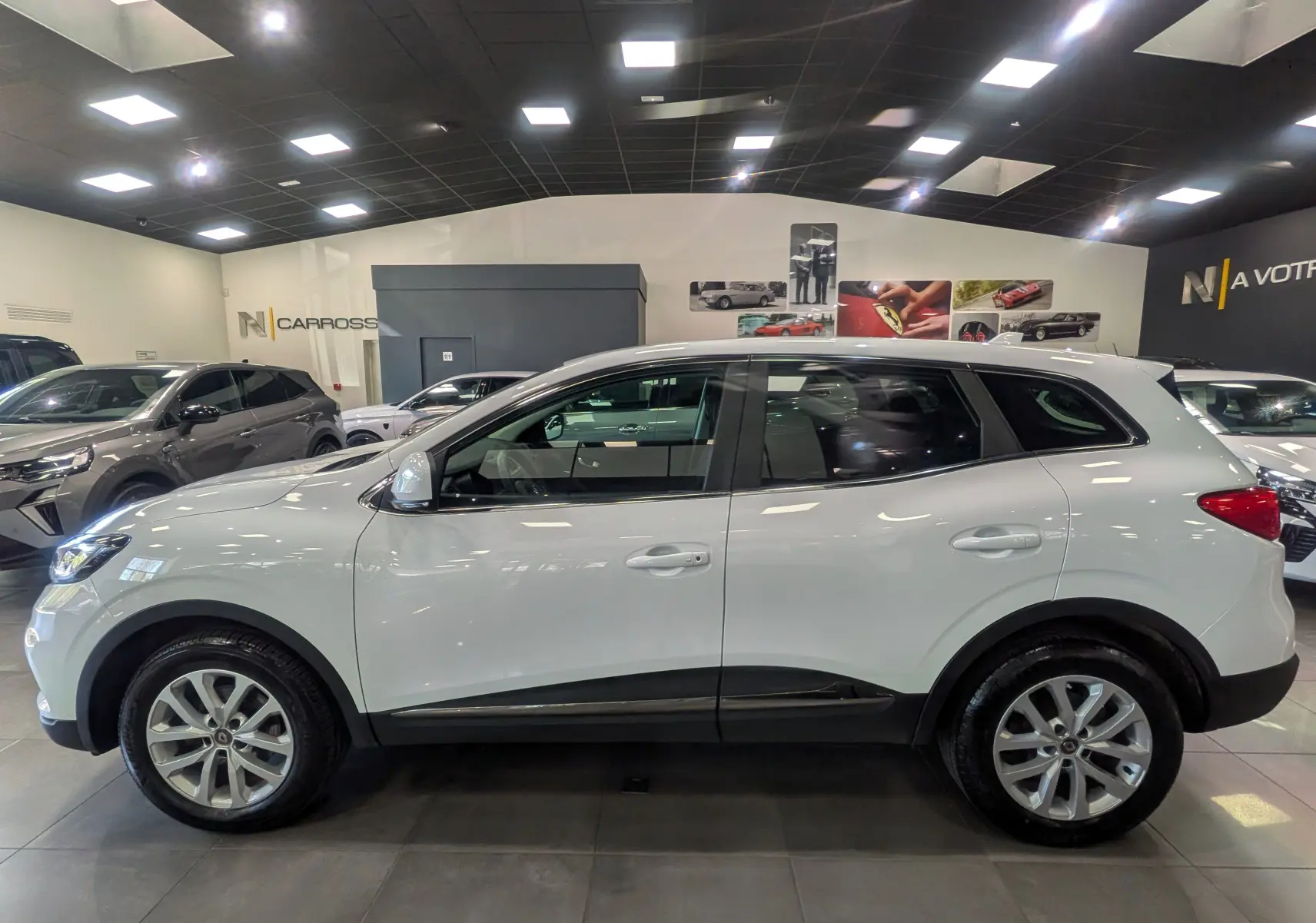 Profil côté gauche d'un Renault Kadjar Blanc Glacier 2021 en showroom, avec jantes alliage et détails noirs sur les bas de caisse.