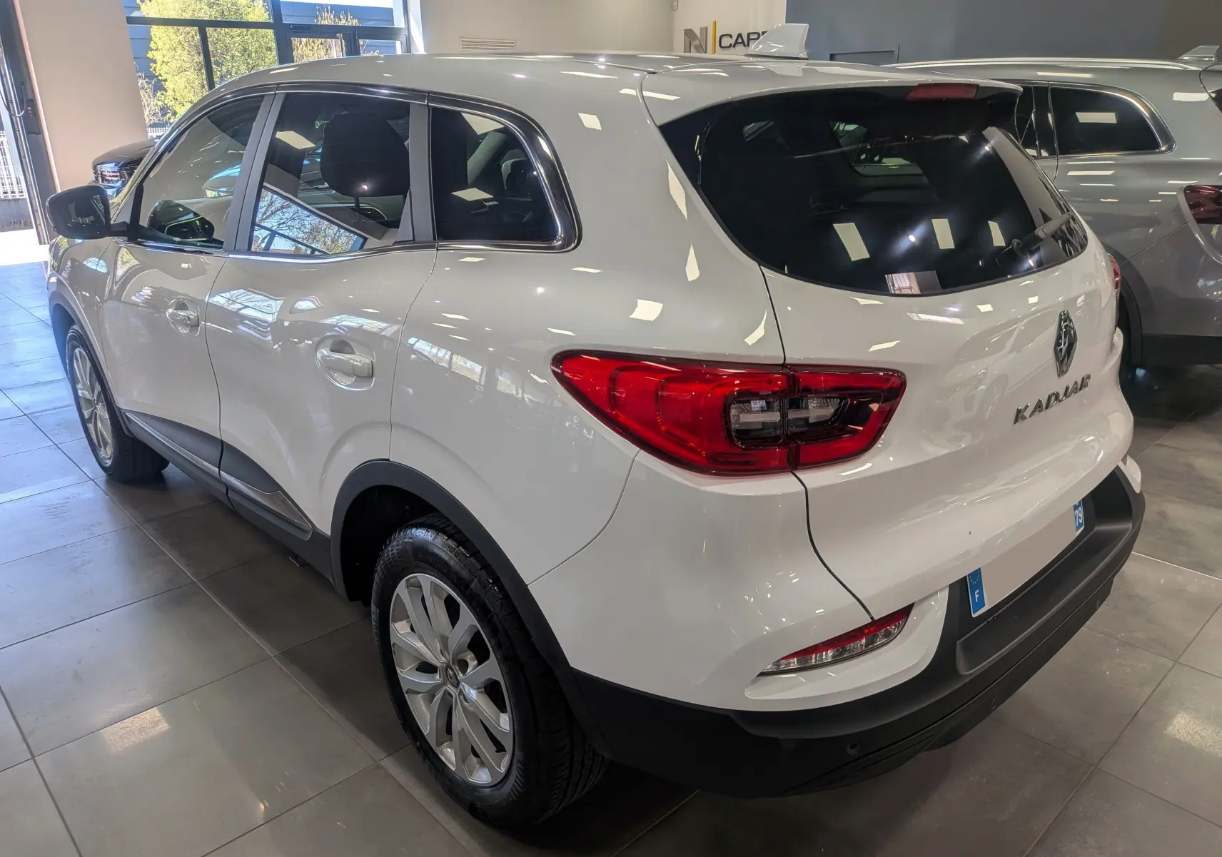 Vue 3/4 arrière droite d’un Renault Kadjar blanc Glacier 2021 en showroom, avec feux arrière et jantes visibles.