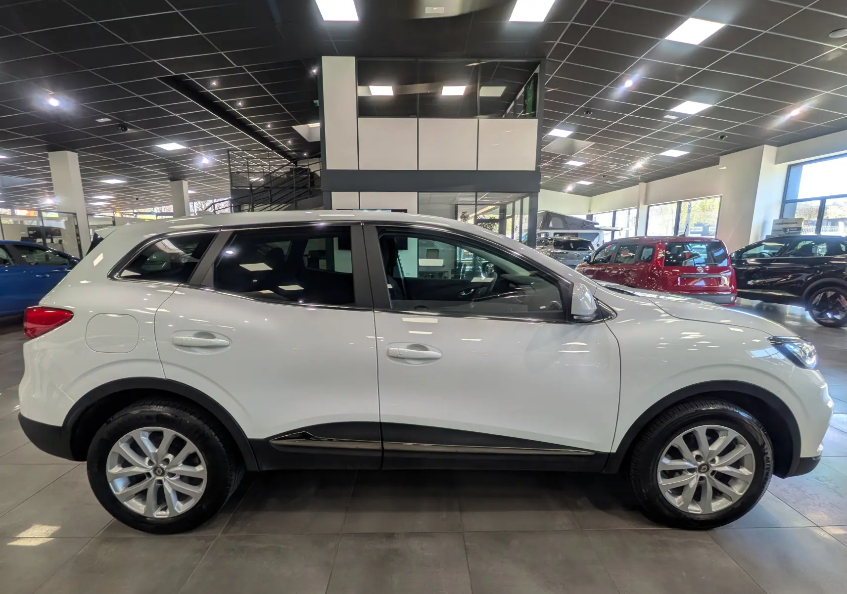 Profil côté gauche du Renault Kadjar blanc Glacier 2021 en version Blue dCi 115 CH BUSINESS, dans un showroom lumineux.