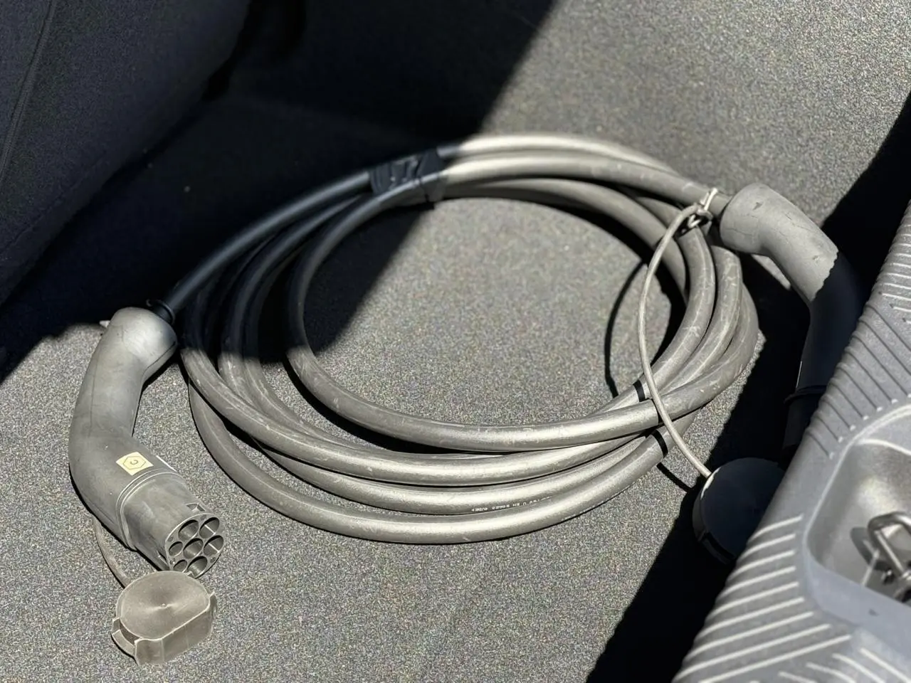 Câble de recharge électrique noir enroulé dans le coffre d'une Renault R5 E-Tech blanc nacré, vue rapprochée.