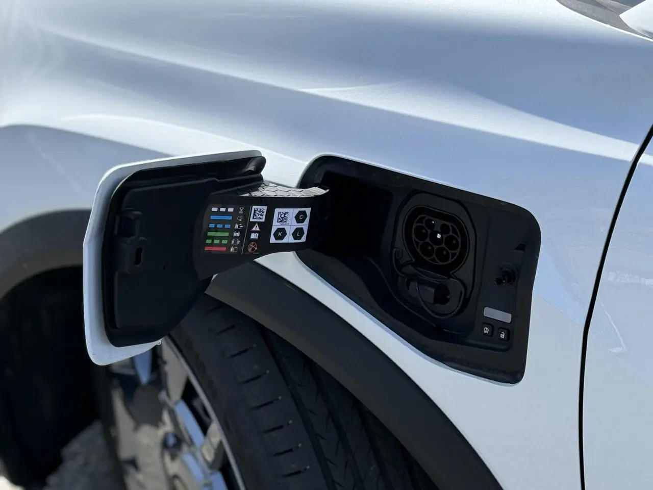 Prise de recharge ouverte côté gauche sur Renault R5 E-Tech blanc nacré, avec jante acier 18 pouces visible.