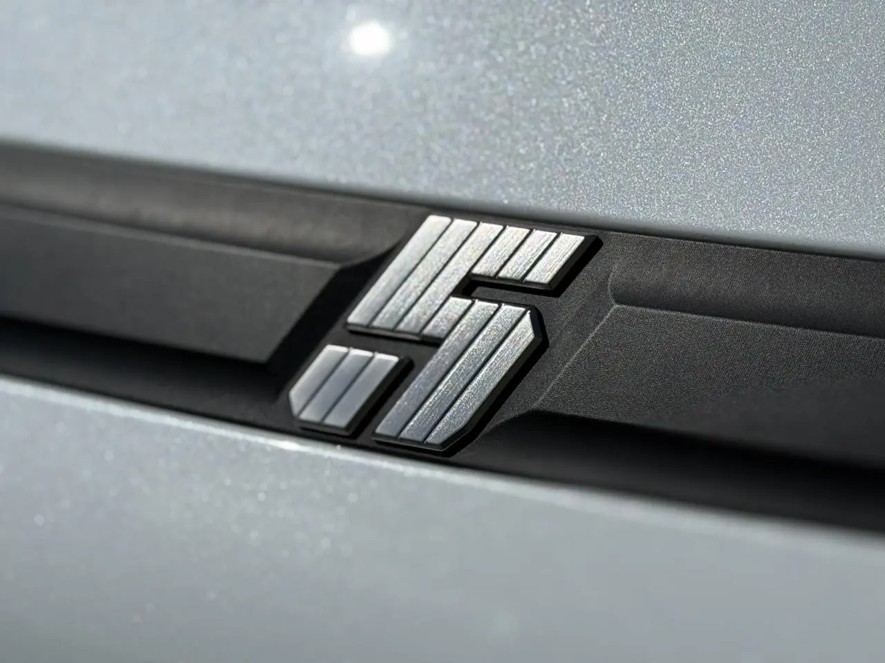 Gros plan sur le logo E-Tech argenté sur fond noir, sur la carrosserie blanc nacré de la Renault R5 électrique.