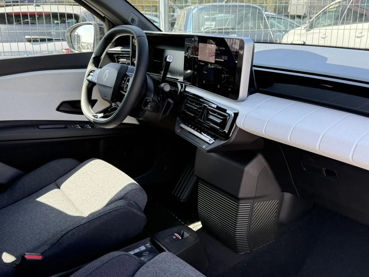 Vue intérieure côté conducteur de la Renault R5 E-Tech 2026, tableau de bord blanc nacré et sièges textile gris matelassé.