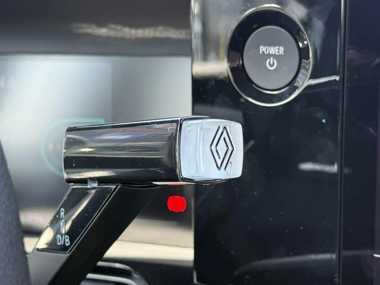 Gros plan sur le levier de vitesses noir brillant avec logo Renault, bouton Power en arrière-plan noir.
