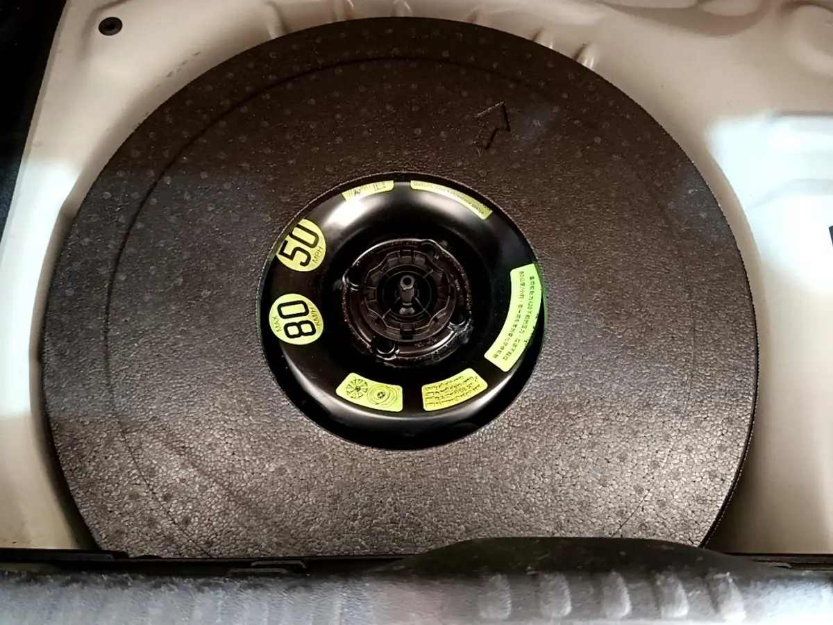 Vue en plongée sur la roue de secours compacte noire dans le coffre d'une Citroën C3 blanche.