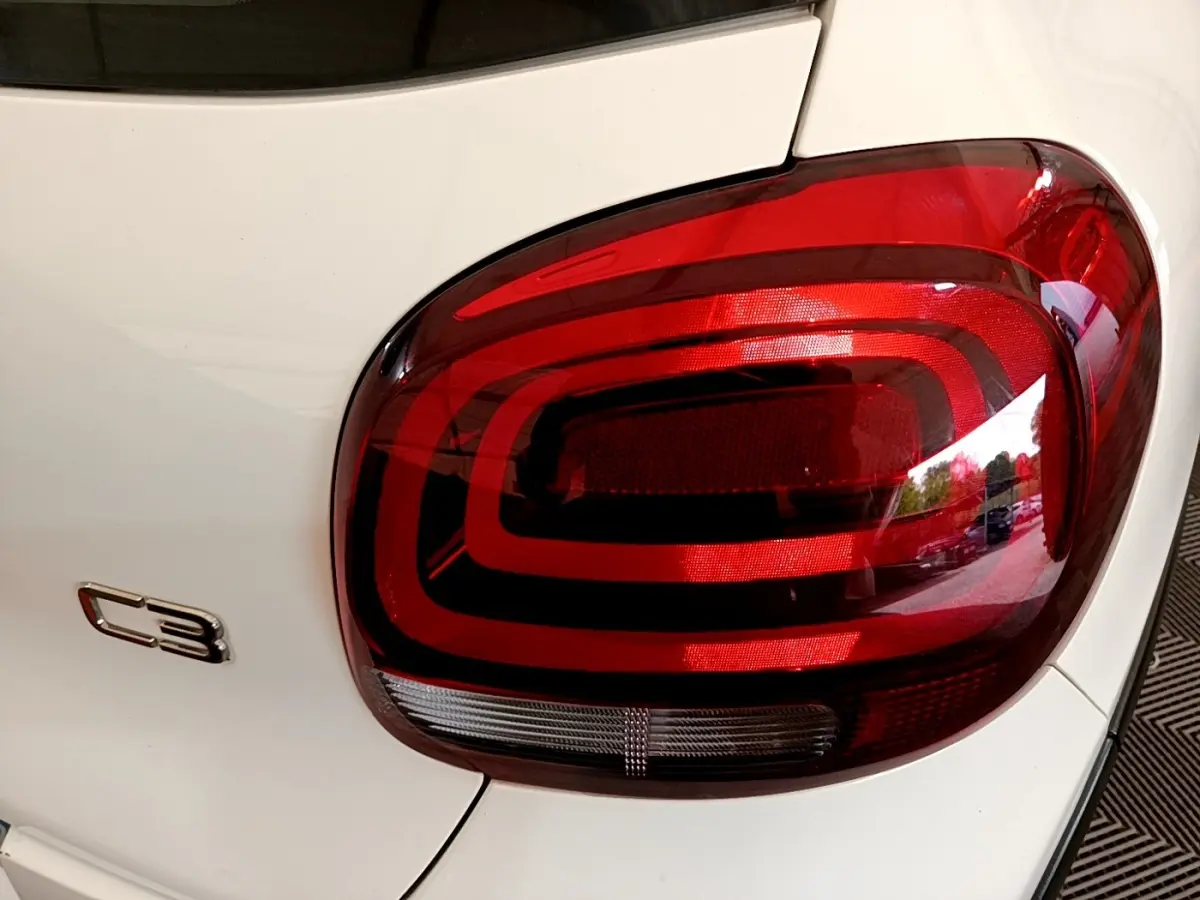 Gros plan sur le feu arrière droit rouge et le logo C3 sur la carrosserie blanche d'une Citroën C3 2021.