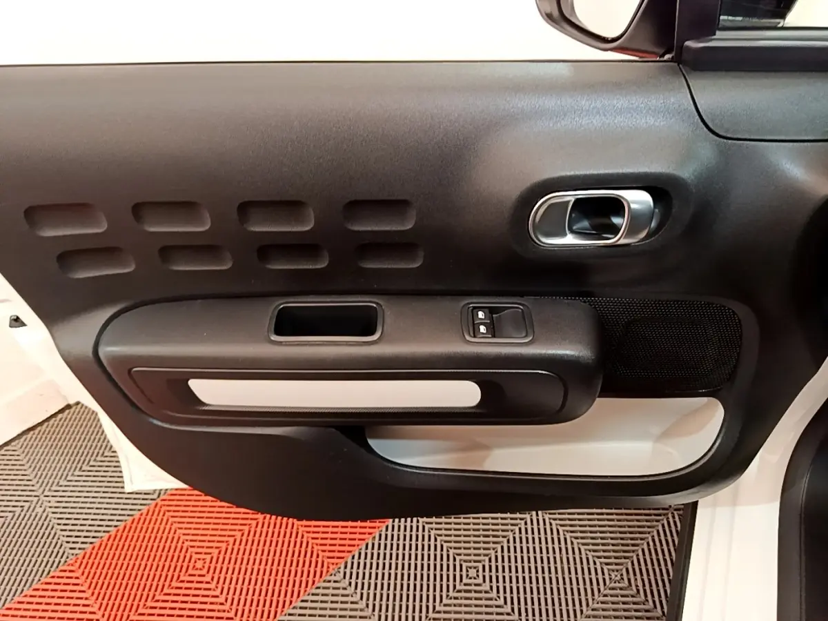 Vue rapprochée de la porte avant gauche blanche de la Citroën C3 avec poignée intérieure chromée et commandes de vitres.