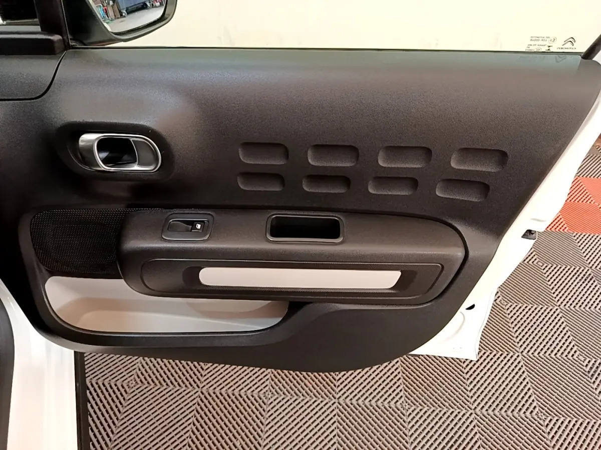 Vue intérieure de la porte côté gauche blanche d'une Citroën C3 2021 avec poignée argentée et panneau noir texturé.