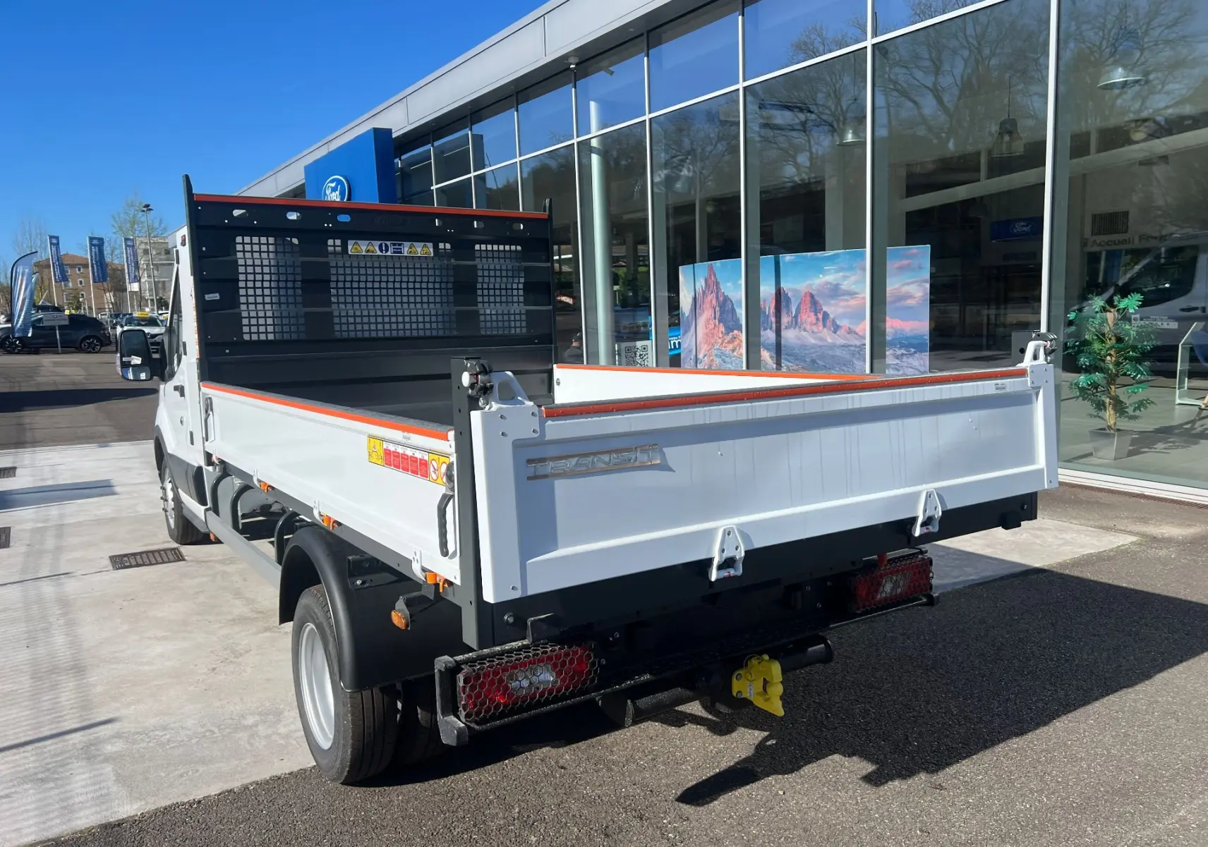 Ford Transit Chassis Cabine blanc vu 3/4 arrière droit, avec benne basculante et coffre, roues jumelées visibles.