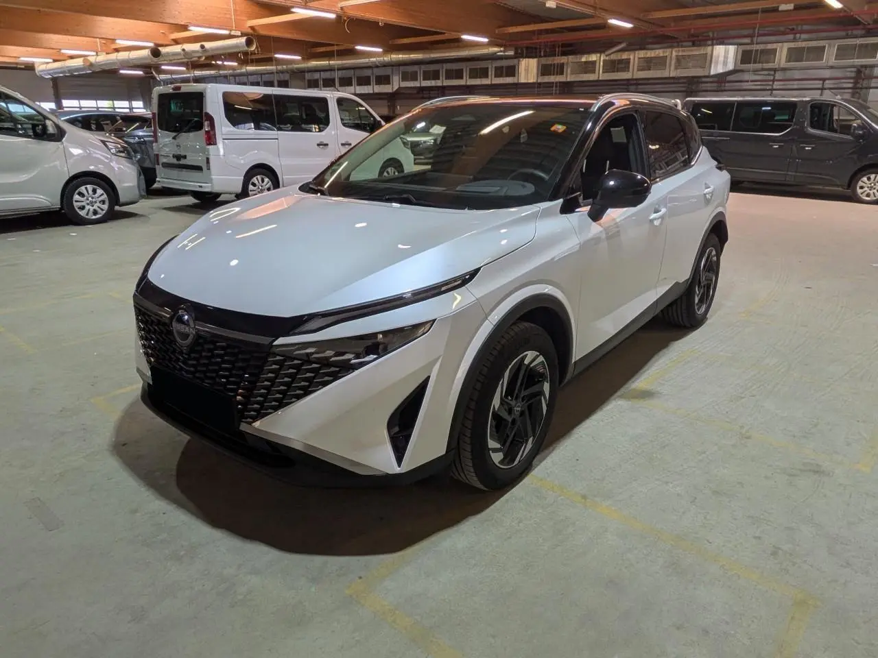 Vue 3/4 avant droit d'un Nissan Qashqai blanc nacré avec toit noir et jantes alliage dans un parking intérieur.