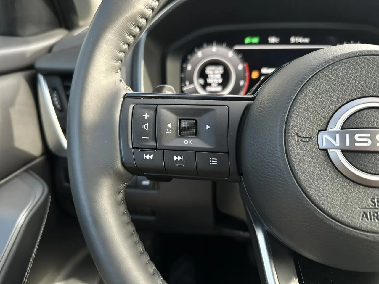 Gros plan sur le volant cuir noir du Nissan Qashqai 2025, avec commandes multifonctions côté gauche et tableau de bord numérique en arrière-plan.