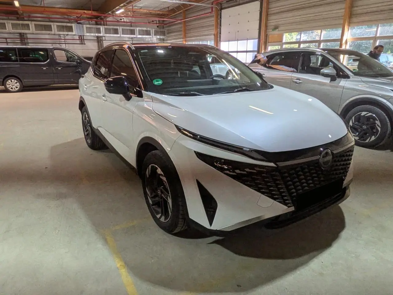 Nissan Qashqai blanc nacré et noir en 3/4 avant droit, avec calandre noire et jantes alliage 18 pouces.