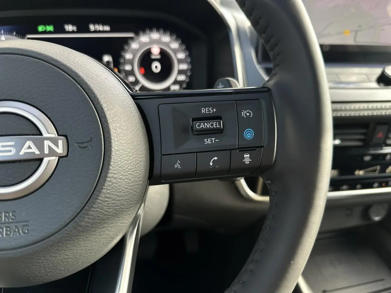 Gros plan sur le volant noir du Nissan Qashqai 2025 avec commandes intégrées et tableau de bord numérique en arrière-plan.