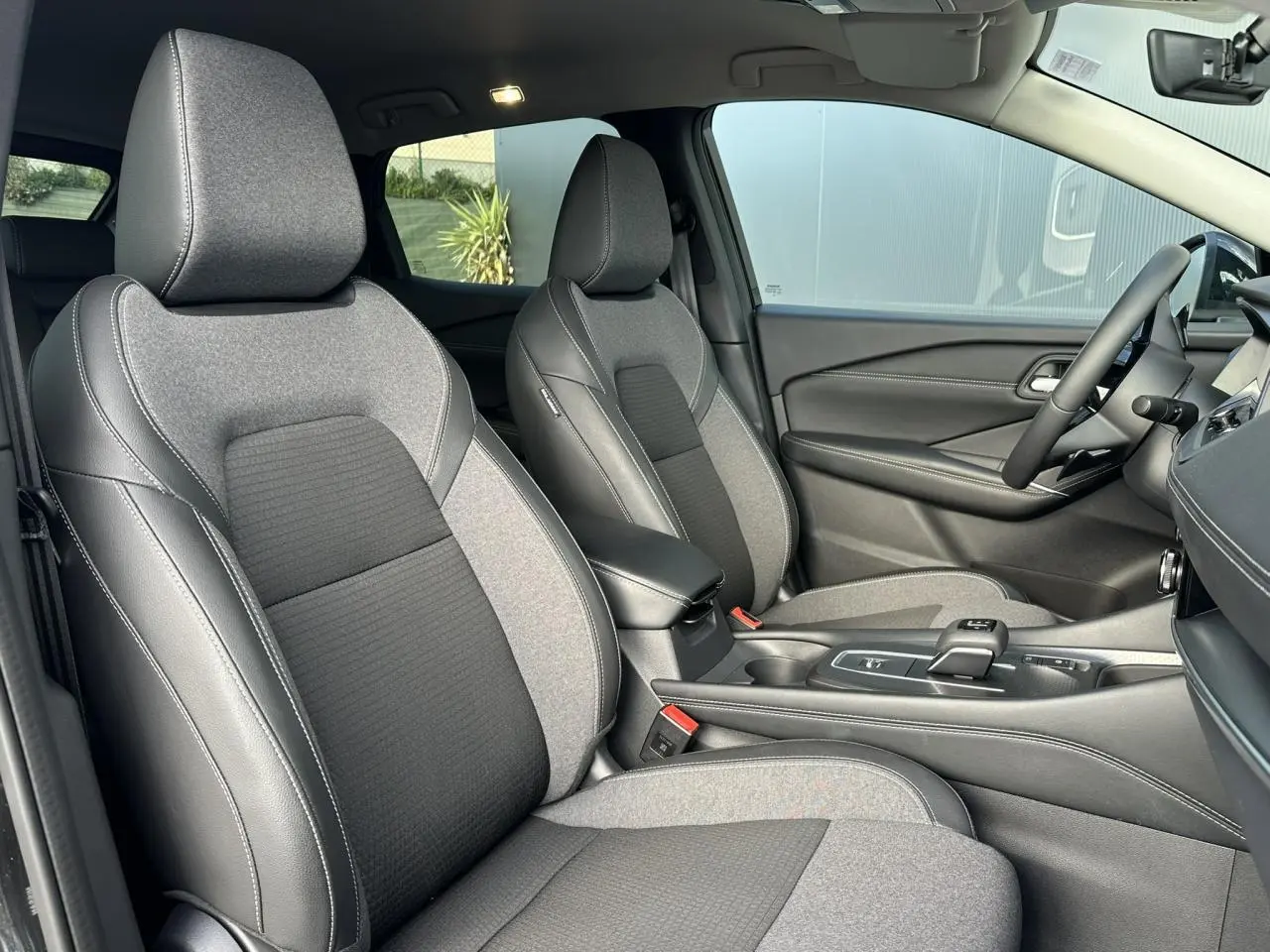 Vue intérieure côté droit du Nissan Qashqai 2025, sièges avant bi-matière gris et noir avec console centrale.