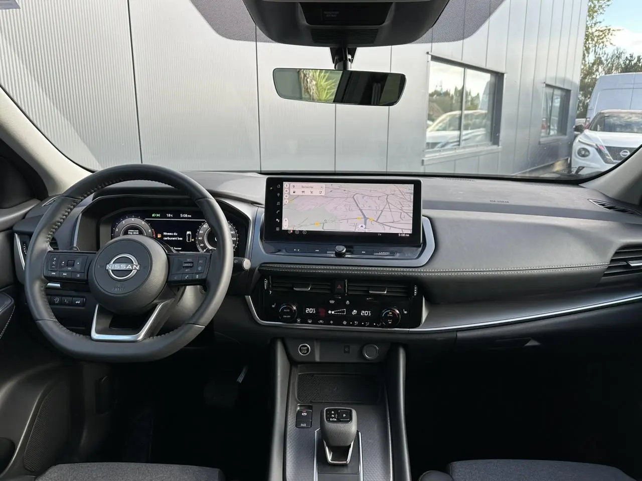 Vue intérieure avant du Nissan Qashqai 2025 avec tableau de bord noir, écran tactile central et volant cuir multifonction.