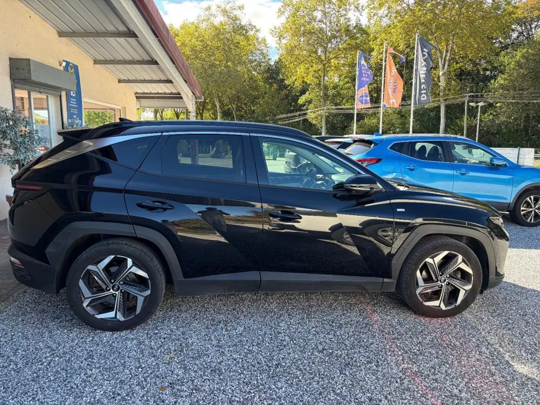 Hyundai Tucson noir vu de profil côté gauche, avec jantes alliage et barres de toit visibles en extérieur.