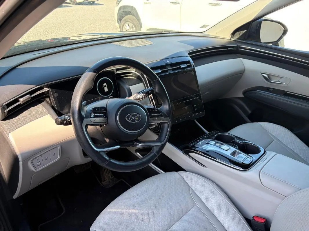 Vue intérieure côté conducteur du Hyundai Tucson 2022, volant cuir, sièges clairs et console centrale avec écran tactile.