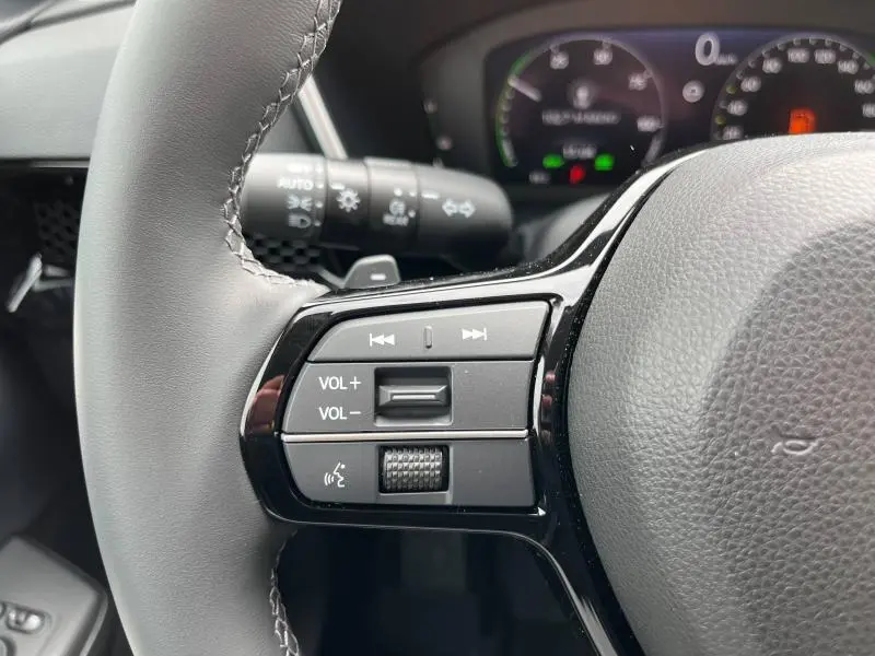 Gros plan sur les commandes audio au volant cuir noir du Honda CR-V 2024 hybride, avec tableau de bord flou en arrière-plan.