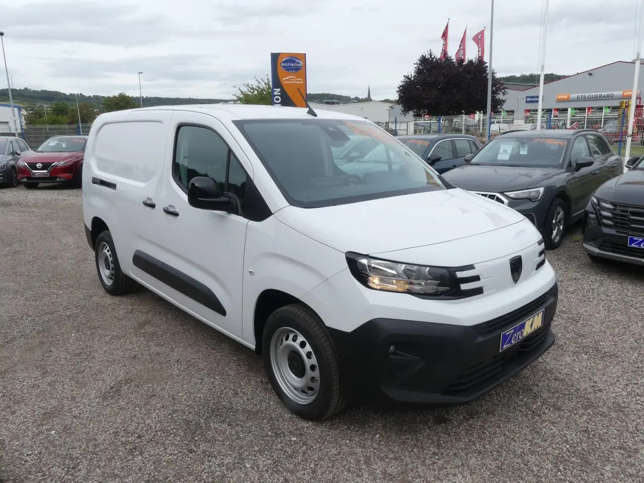 Peugeot Partner blanc vue 3/4 avant droit avec boucliers noirs et jantes tôle grises sur parking.