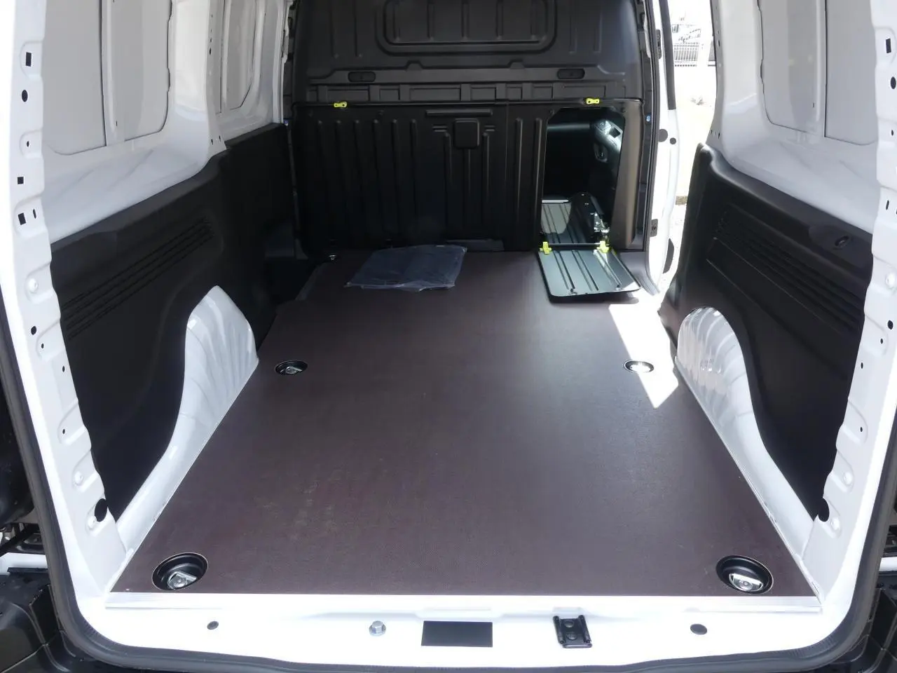 Vue intérieure arrière du Peugeot Partner XL blanc 2025 montrant le plancher bois antidérapant et les anneaux d'arrimage au sol.