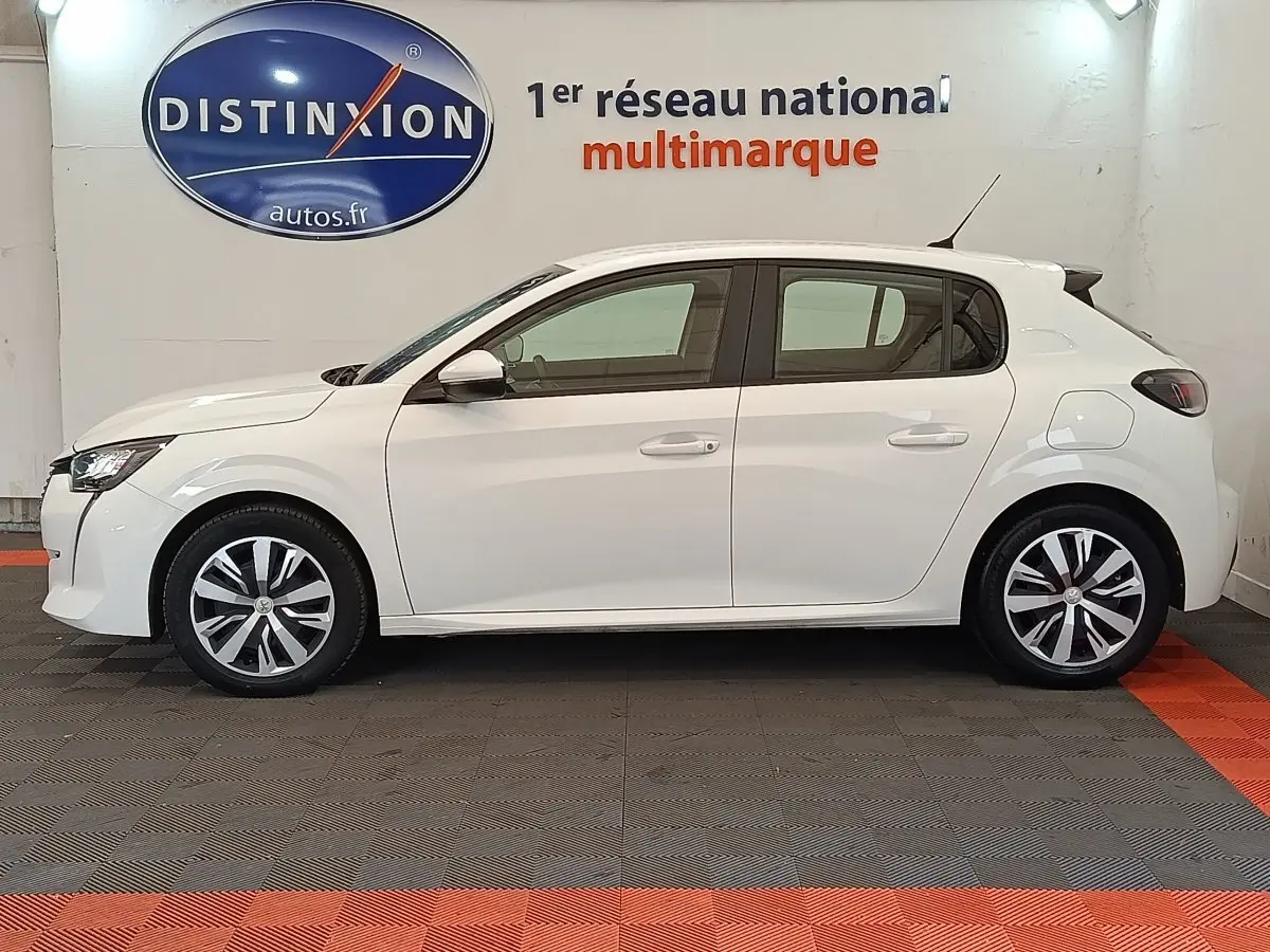 Profil latéral droit d'une Peugeot 208 blanche 2020, avec jantes alliage et rétroviseurs blancs dans un showroom.