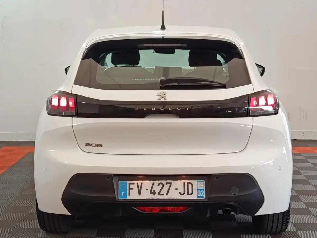 Vue arrière d'une Peugeot 208 blanche de 2020 avec feux LED allumés et logo Peugeot central sur hayon noir.