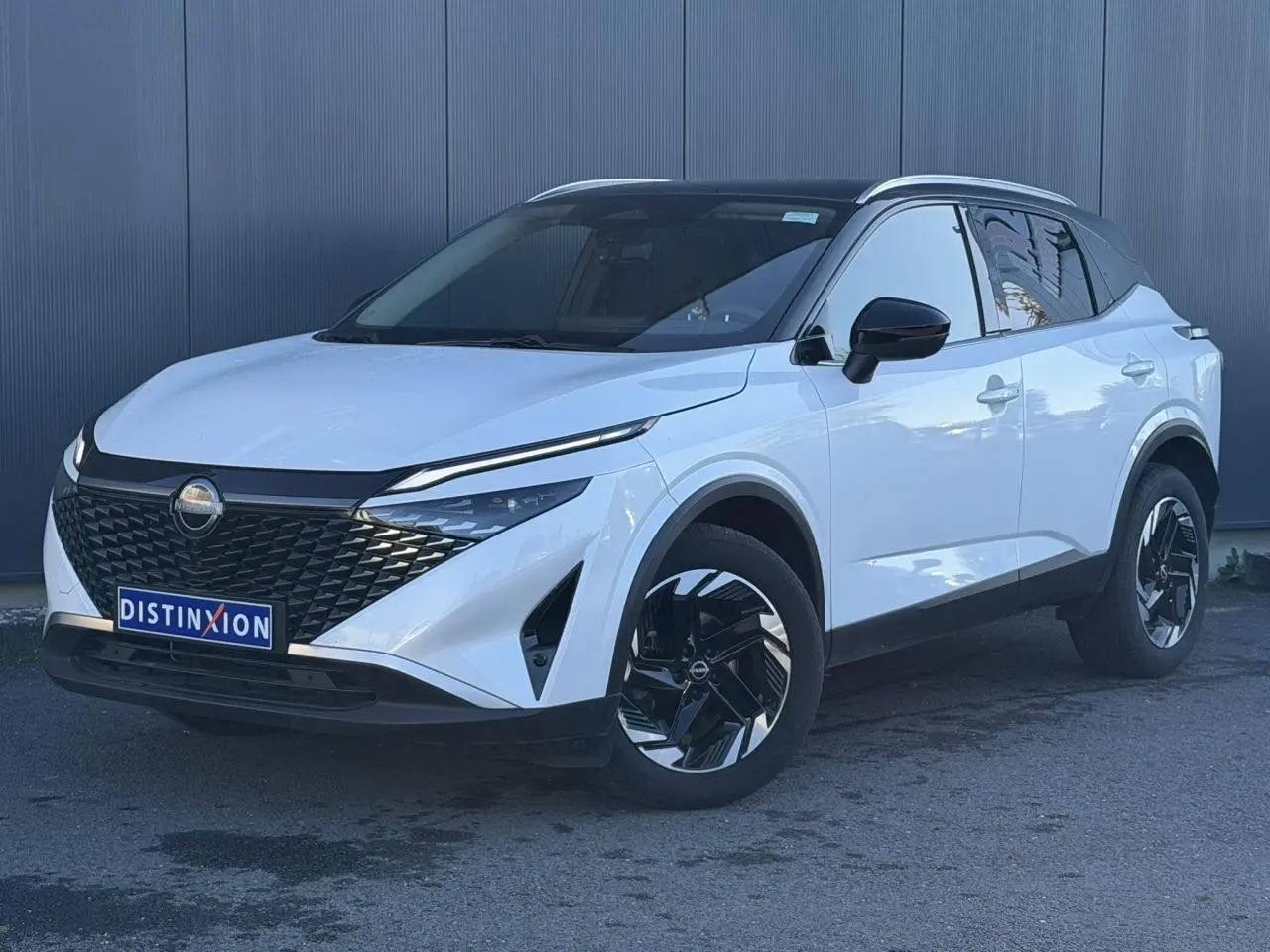 Nissan Qashqai 2025 blanc nacré avec toit noir, vue 3/4 avant droit, jantes alliage noires et calandre distinctive.