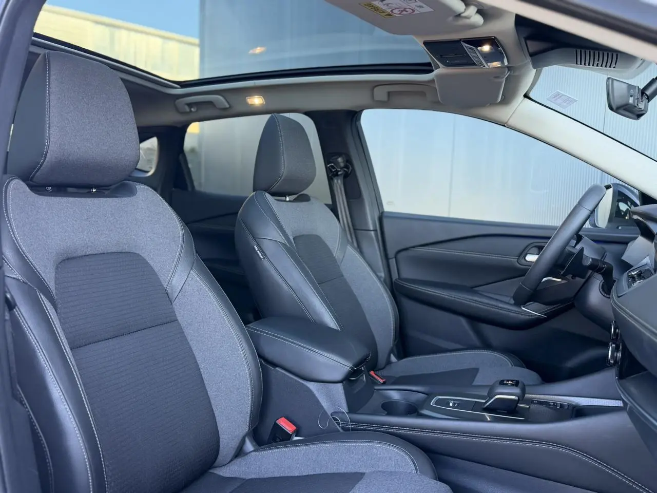 Vue intérieure côté droit du Nissan Qashqai 2025, sièges bi-matière gris, toit panoramique en verre ouvert.