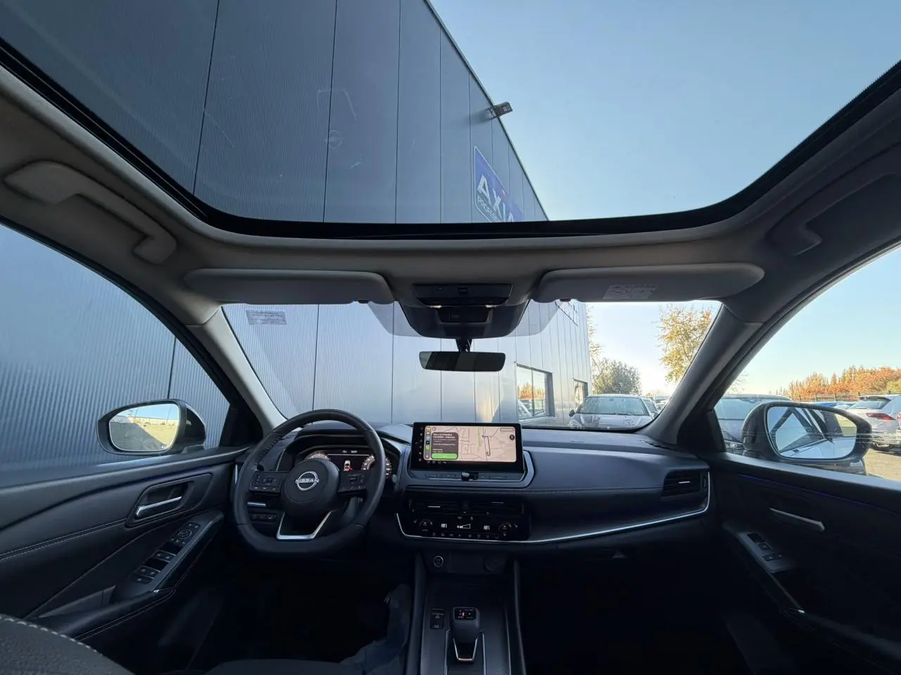Vue intérieure avant du Nissan Qashqai 2025 avec toit panoramique en verre, tableau de bord numérique et écran tactile central.