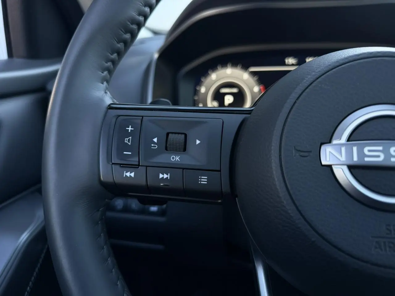 Gros plan sur le volant cuir noir du Nissan Qashqai 2025 avec commandes multifonctions et tableau de bord numérique flou.