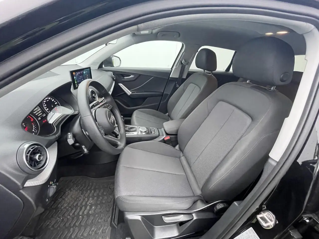 Vue intérieure côté conducteur de l'Audi Q2 noir mythic 2023, sièges tissu gris et tableau de bord moderne.